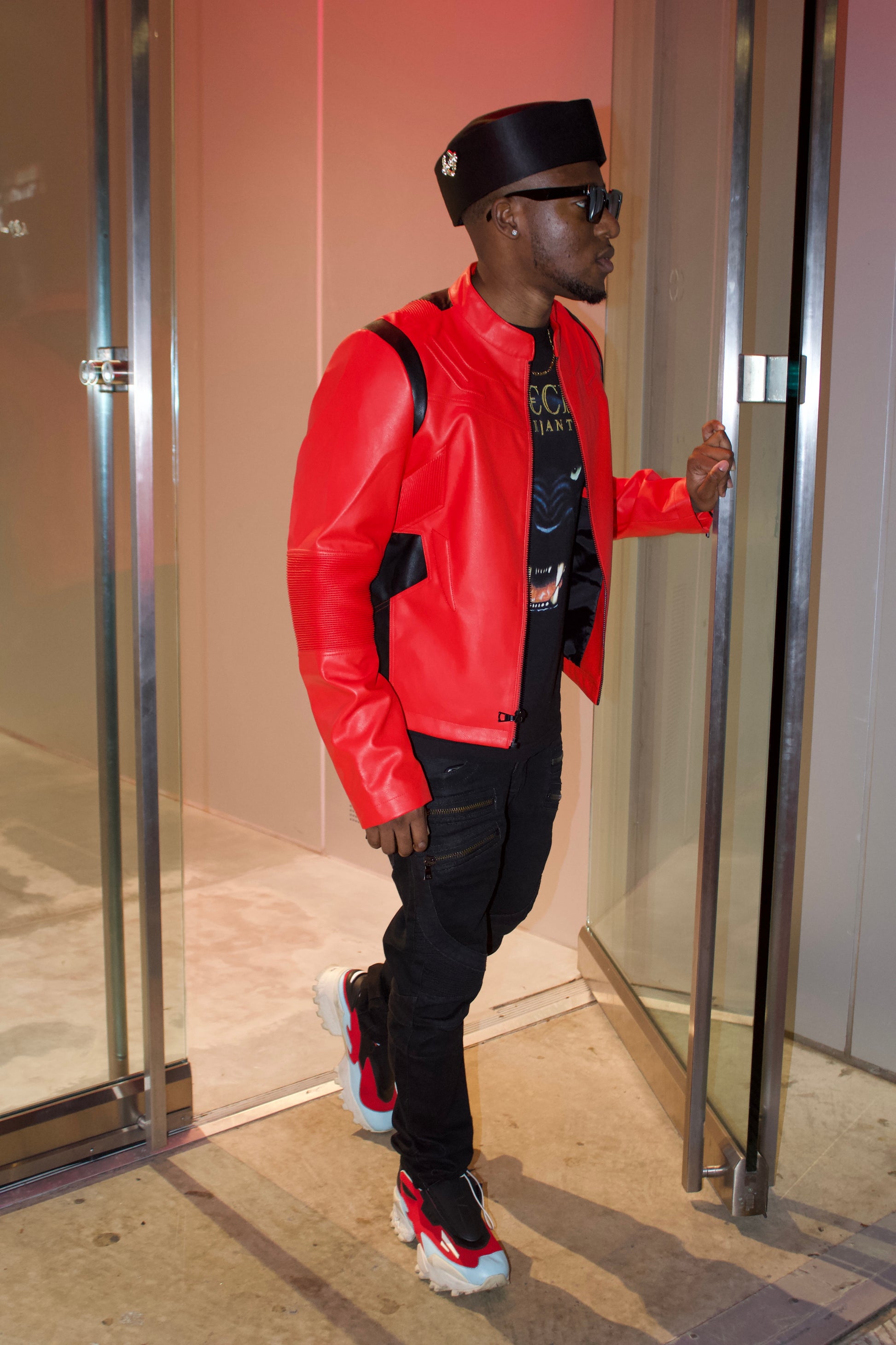 Man in a red jacket and black cap entering a building.