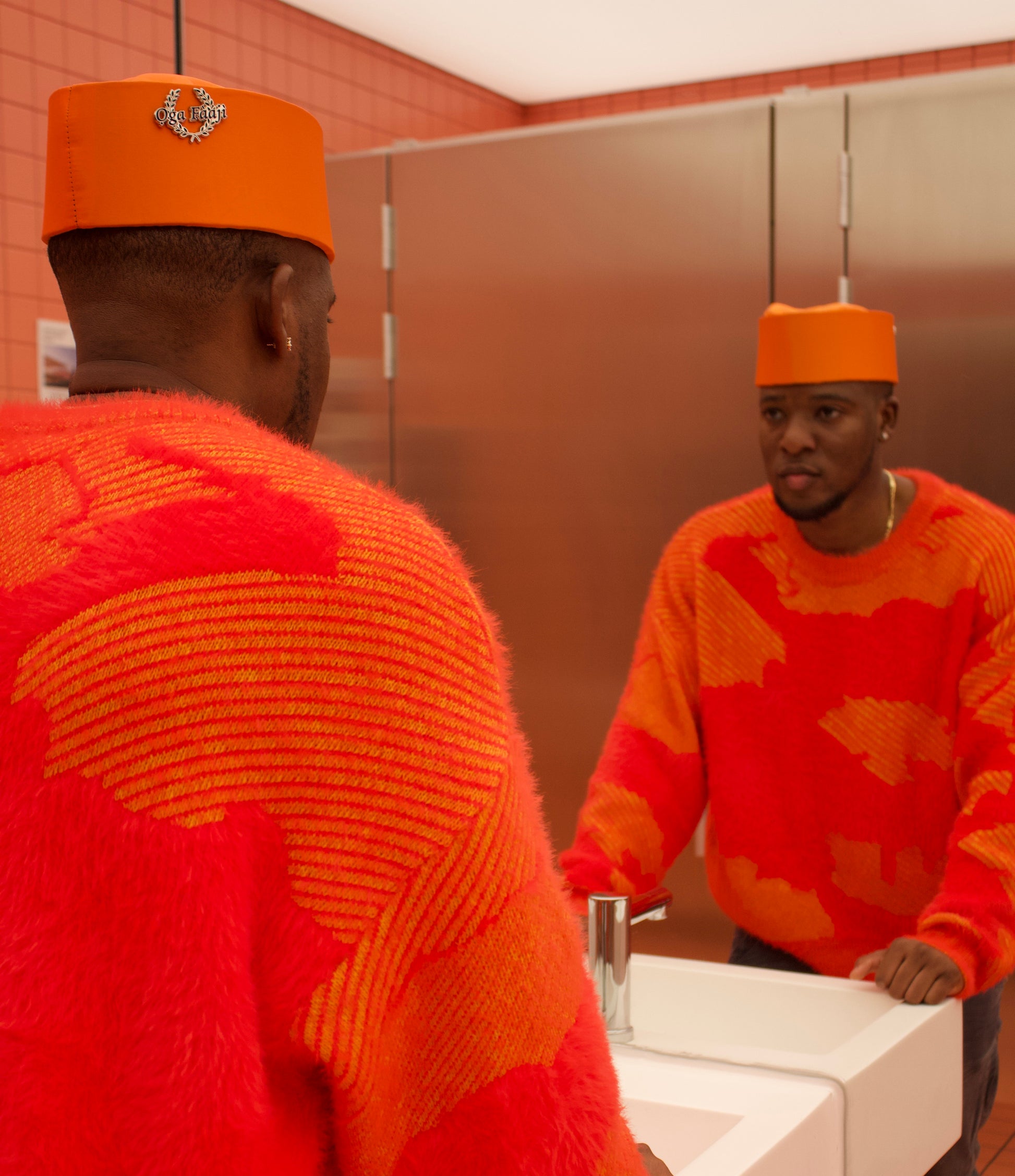 Man wearing an orange hat and sweater looking at himself in a mirror.